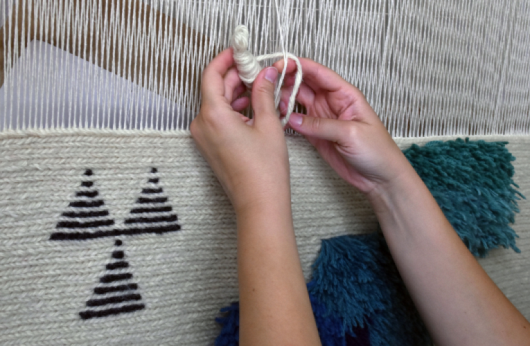 A person hand-weaving a tapestry on a loom, carefully crafting intricate patterns with colorful threads.